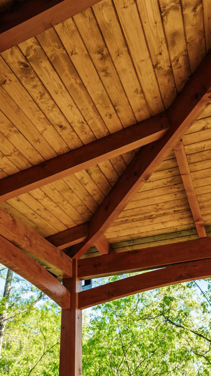 Rustic hybrid timber frame home with natural wood interior set amidst lush green trees.