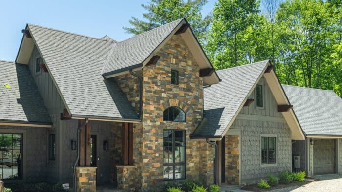 A stunning custom log cabin home with natural stone accents, set in a lush, wooded mountain landscap.